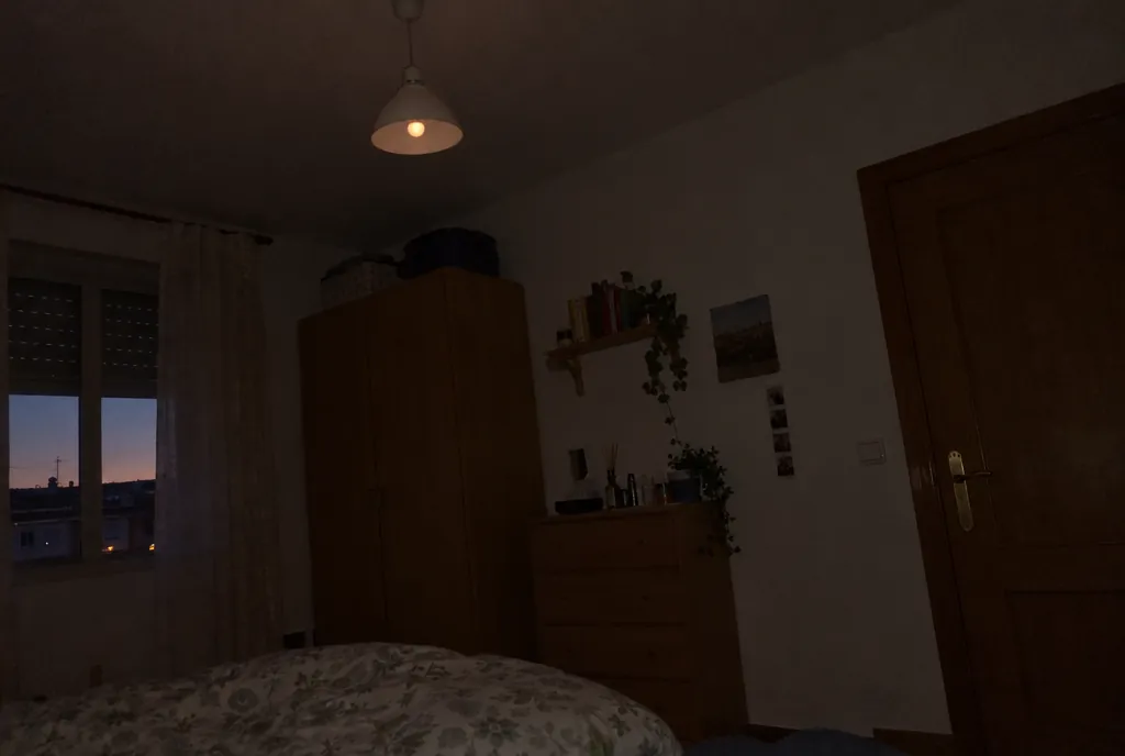 Dormitorio en penumbra con la luz apagada y la bombilla LED de la lámpara de techo emitiendo un brillo débil