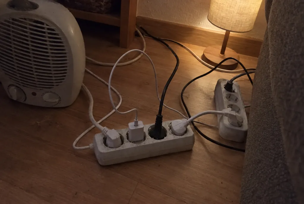 Regleta de cuatro enchufes en el suelo de un salón con un calefactor, un cargador, una lámpara y otra regleta conectada a ella